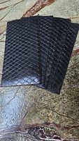 Five black non-slip traction pads stacked on stone surface showing diamond textured pattern