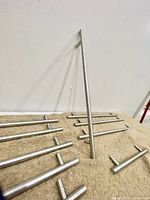 Photo showing a set of chrome finish kitchen cabinet handles arranged on a beige carpet with some leaning against a white wall. Handles appear polished and tubular with short mounting posts.