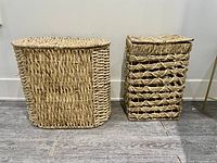 Two handmade woven wooden laundry hampers, showing their front view on a hard floor against white wall.