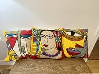 Front view of three square pillows with colorful abstract Picasso-style face prints