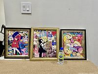Photo showing all three framed pop art prints side by side on a floor against a wall, with a water bottle for scale.
