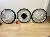 Front view of three retro wall clocks, each black framed and about 19x19 inches, placed on floor with soda can for size reference.