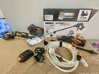 Lot overview showing Hydroshot pressure washer box, nozzles, hose, battery, charger, cordless jigsaw and angle grinder