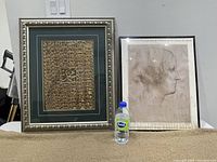 Photo showing two framed art pieces side by side with water bottle for scale.