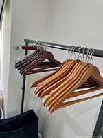 Hangers on a black metal clothing rack; light wood and dark wood hangers including pant hangers with clips visible.