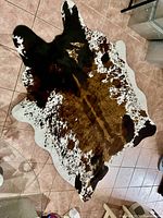 Brown, black, and white splotched cowhide patterned rug with irregular edges laid on tiled floor, showing front and overall pattern