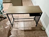 Front view of small modern desk with wood top and black metal frame including mesh side panel and caster wheels.