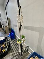 Two crochet macramé cream colored plant holders hanging, each holding a small artificial plant (green succulent and yellow flower).