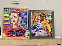 Two framed pop art prints side by side on a surface, with bottle for scale