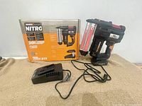 Tool, charger and original box arranged side by side on beige surface