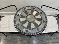 Top view of round patio table with ceramic mosaic tile top and edges showing two chairs with cushions.