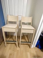 Two wooden bar stools placed side by side, facing forward showing seat and backrest.