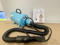 Blue metal high pressure pet hair dryer with flexible black hose, visible on carpeted floor.