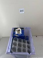 Box of white LED tea light candles packed in blue boxes and placed inside a purple plastic storage bin.
