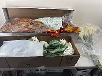 Lot of artificial flowers and autumn leaves in boxes and packs showcasing all items included.
