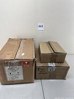 Three cardboard boxes stacked on a floor against a wall, labeled with contents. The boxes appear used and marked fragile.