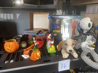 Shelf displaying various Disney collectibles including Halloween themed pumpkin candle holders, figurines, lanyard, and boxed Blu-ray set.