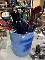 Photo showing large blue barrel filled with assorted golf clubs, visible covers on some clubs.