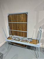 Blue metal framed wooden table and one bench lying on its side with folded legs on bench.