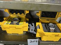 Both Invicta watches in separate yellow protective cases with foam inserts, showing one with gold and white face, and the other with black face.