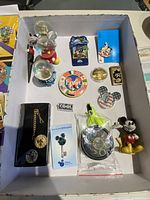 Box with assorted enamel Mickey Mouse collectible pins, decorative keychains, coin, and a bobblehead figurine