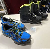 Pair of blue New Balance composite toe sneakers and black Orvis snow boots together on a table