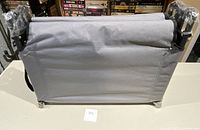 Compact folded Ozark Trail collapsible cot showing gray fabric and metal legs with plastic wrapping on ends.