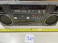 Front view of Panasonic RX-C39 boombox showing cassette player, radio tuner, speaker grills, control knobs, and buttons with a tape measure indicating size.