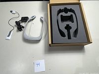 PoNS neurostimulation device and accessories laid out on a table, including charger, power adapter, communication cable, and black foam insert box.