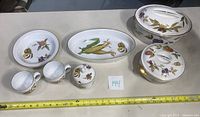 Full set of Royal Worcester Evesham Gold dinnerware laid out on table, showing all items including oval and circular covered casserole dishes, two cups, sugar bowl, serving dish and bowl.
