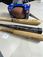 Photo showing three signed baseball bats including a black and natural wood Louisville Slugger bat, two natural wood Rawlings Big Stick bats, and a signed football in an original Wilson box.