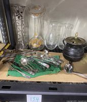 Photo showing mixed sterling and stainless flatware, multiple glass vases including two vintage painted glass vases with yellow floral decoration, and black cast iron pot with brass lid and ladle
