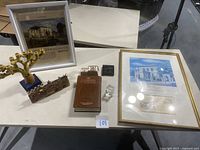 Photo showing entire lot on white table with framed items, menorahs, dreidel, paperweight, ceramic sculpture, and siddur