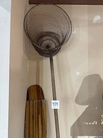 Full view of vintage metal fish net hanging on wall showing circular wire mesh net and 6-foot pole