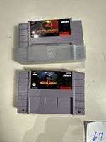 Photo showing two Super Nintendo cartridges of Mortal Kombat 1 and Mortal Kombat 2, both with original label artwork and plastic cartridge protectors on one cartridge.