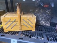 Vintage wooden expandable sewing box on a metal shelf, showing exterior and handle with visible wear and scratches.