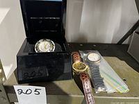 Three watches on shelf: skeleton leather strap, skeleton in case, matte black watch in bag