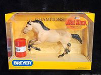 Boxed model horse figure named Hot Shot, accompanied by a red and white barrel accessory. Yellow box with clear plastic front.
