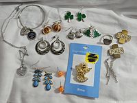 Overview of assorted costume jewelry laid out on a white cloth, showing necklaces, earrings, bracelet, and brooch.