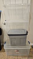Stack of four assorted storage totes, including three clear plastic totes and one gray tote, all with lids.