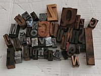 Top view of assorted vintage printing blocks showing a variety of reversed letters, numbers, and symbols made of wood and metal.