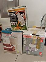 Image showing three vintage kitchen appliances in their original boxes: Presto Salad-Shooter, Soft Serve Ice Cream Machine, and Singer Electric Slicer