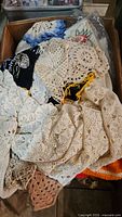 Box filled with mixed vintage linen and crochet doilies in cream and beige tones, assorted sizes and patterns.