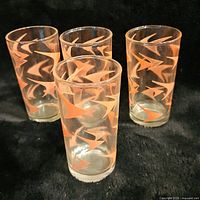 Four clear cylindrical glasses decorated with orange and white atomic boomerang pattern.