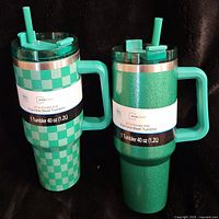 Two 40 oz Mainstays stainless steel tumblers shown side-by-side, one with green checkered pattern and the other textured green, both with handles and straws.