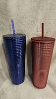 Pair of tall tumblers with textured grid design, one blue and one red, with matching straws.