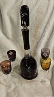 Overall view of vintage dark glass decanter with stopper surrounded by four colored stemmed glasses with cut designs
