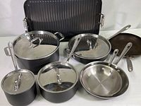 Overview of All-Clad cookware set arranged with grill pan at back, stock pot center, sauce/sauté pans and skillets in front