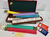Full view of the Cardinal Mah Jongg set displaying the open locking storage case, five colorful plastic tile racks with metal clasps, some game tiles showing traditional designs, printed rules booklets, and the case key.