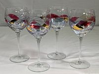 Four Cornet Barcelona art wine glasses with colorful swirl and gold overlay design arranged in a row.
